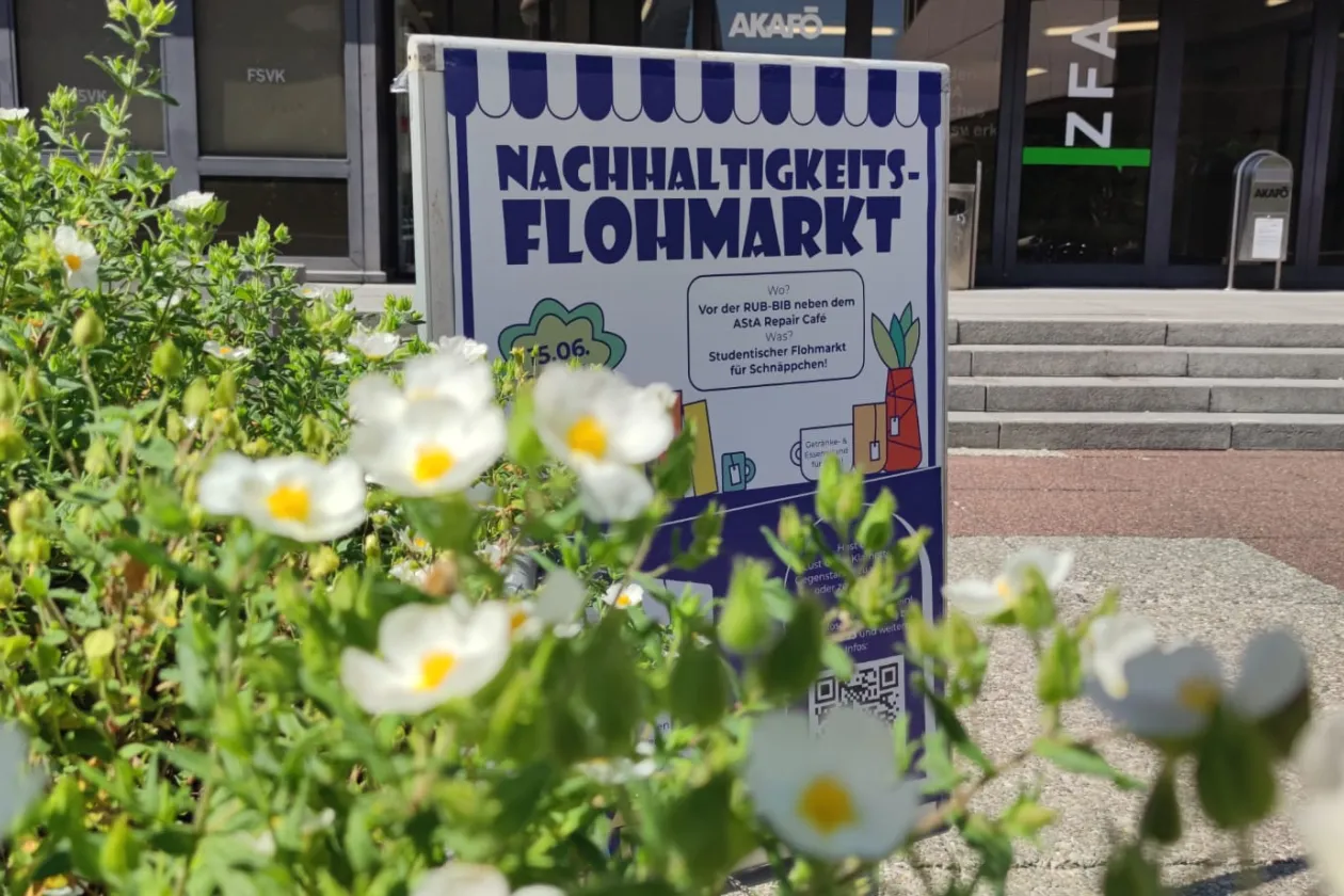 Ein Plakat wirbt für den Nachhaltigkeitsflohmarkt, im Vordergrund Blumen