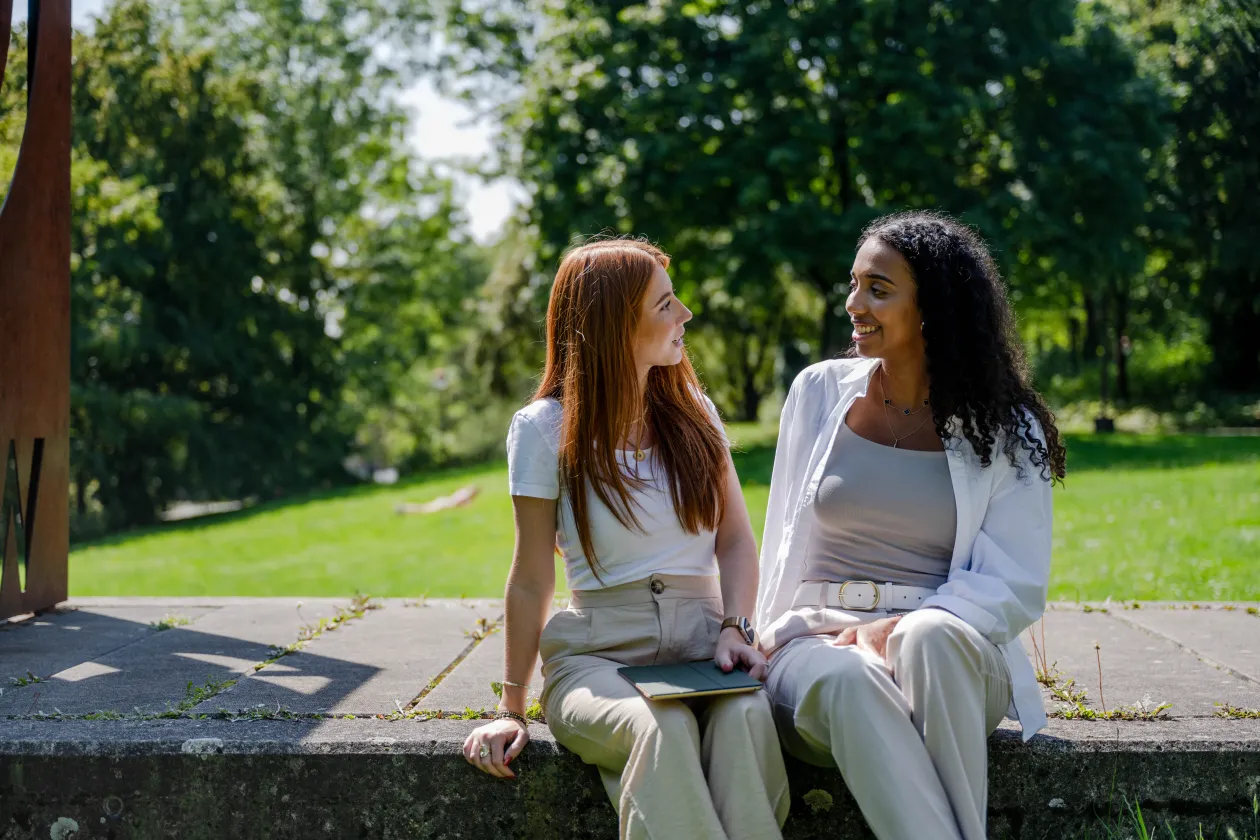Zwei Studierende unterhalten sich auf der Wiese vor dem Restaurant Q-West