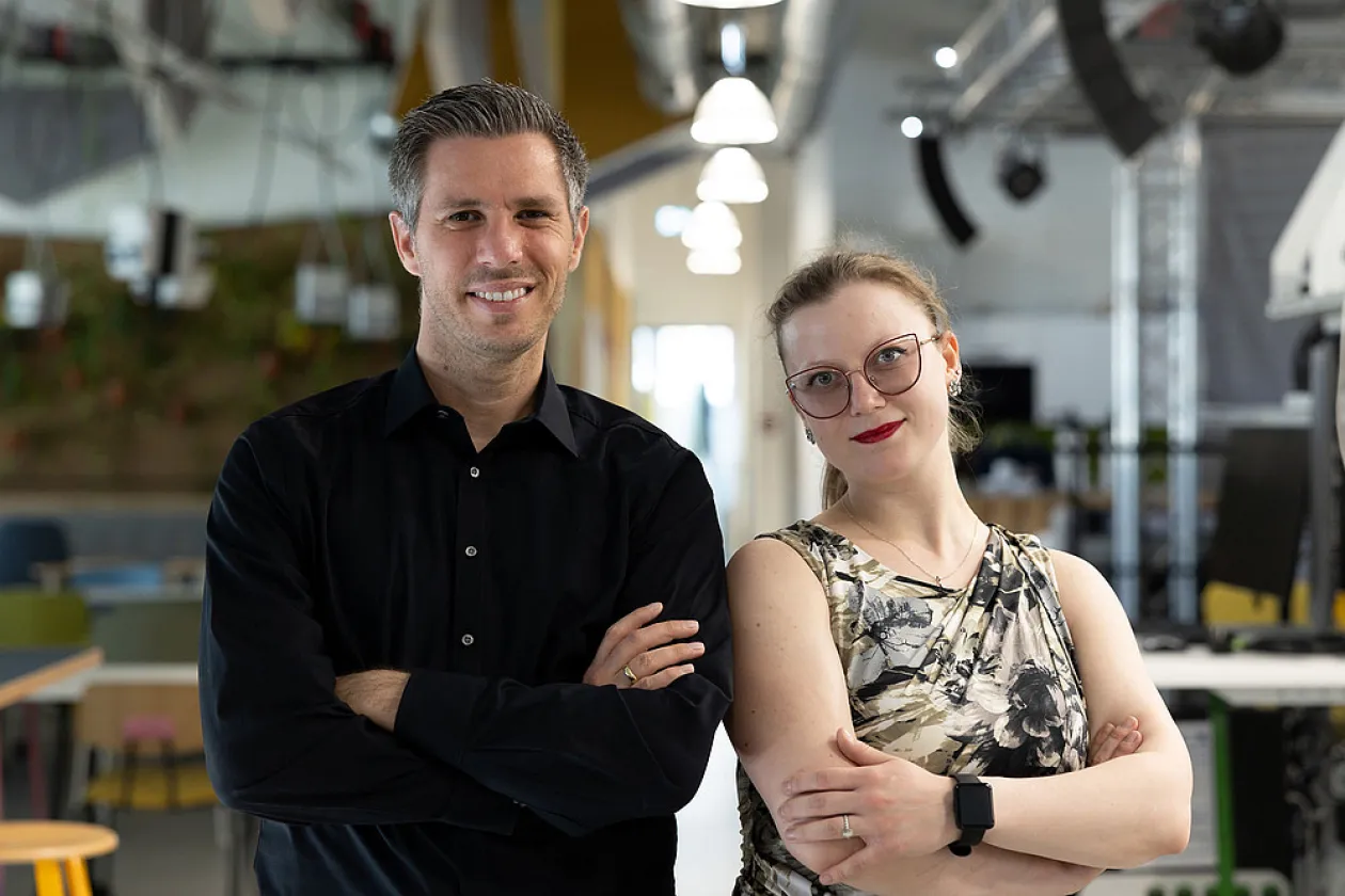 Ein jungerPorträt von Gründer mit schwarzem Hemd und einer Gründerin im armfreien Top.