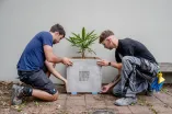 Zwei Männer knien rechts und links eines Betonblumenkastens