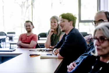 Fünf Menschen sitzen am Tisch und diskutieren lächelnd